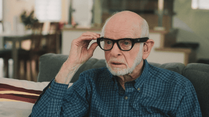 Close-up of an older male user tactilely pressing the physical control button on the right side of the AGIGA smart glasses to activate a command.