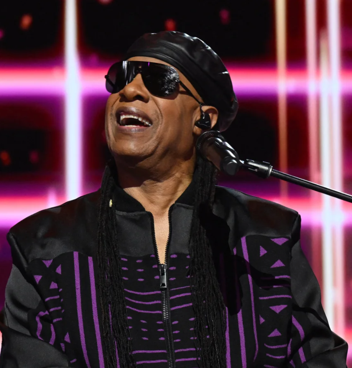 Stevie Wonder singing into a microphone with a vibrant, colorful background