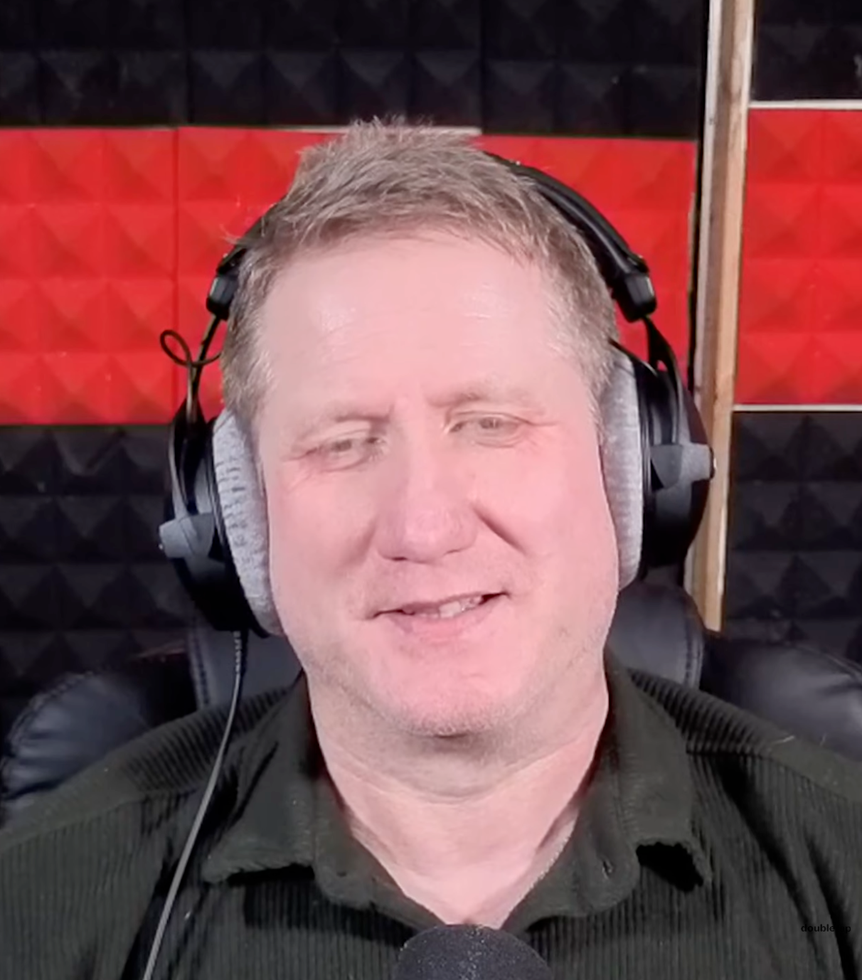 Man wearing headphones in a studio setting with red and black acoustic panels.
